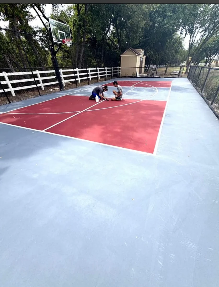 Red and gray outdoor sport court with workers applying court markings