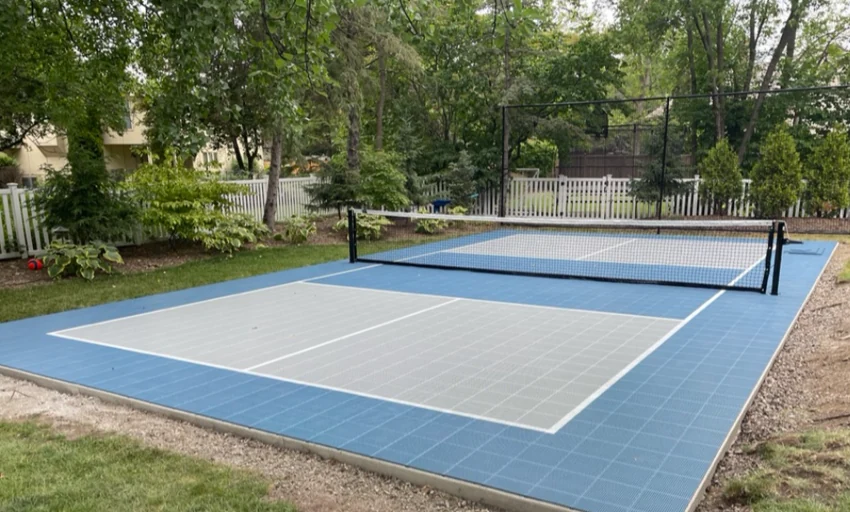 Green backyard pickleball court framed by trees and stone landscaping
